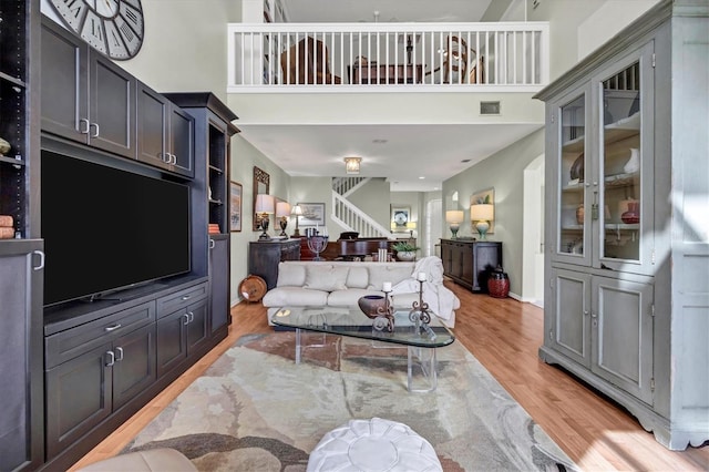 living area featuring light wood finished floors, visible vents, baseboards, stairway, and a high ceiling