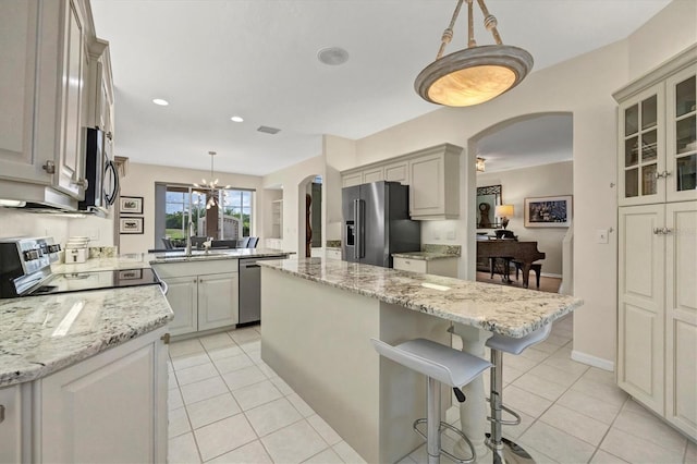 kitchen featuring stainless steel appliances, pendant lighting, light tile patterned floors, a kitchen island, and a breakfast bar