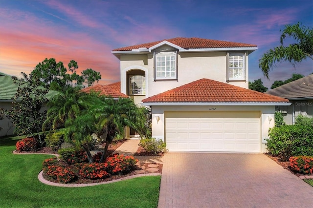 mediterranean / spanish-style house featuring a garage, a tiled roof, decorative driveway, a lawn, and stucco siding