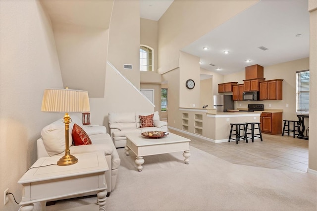 living area with light carpet, light tile patterned flooring, visible vents, and a high ceiling