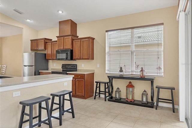 kitchen featuring black appliances, a kitchen bar, visible vents, and brown cabinetry