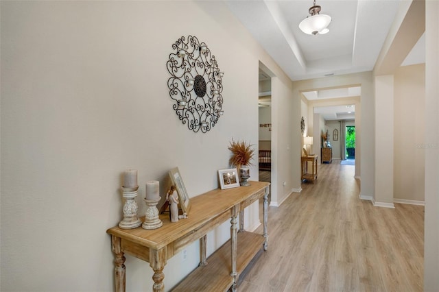 hallway featuring a tray ceiling and light hardwood / wood-style flooring