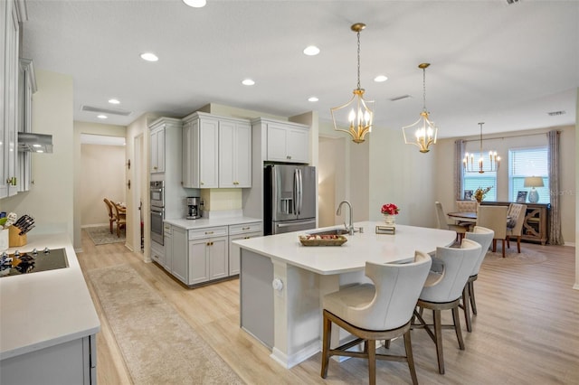 kitchen featuring stainless steel appliances, an island with sink, light wood-type flooring, a breakfast bar, and decorative light fixtures