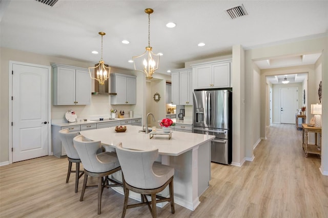 kitchen featuring a breakfast bar, stainless steel fridge, hanging light fixtures, a center island with sink, and black electric cooktop