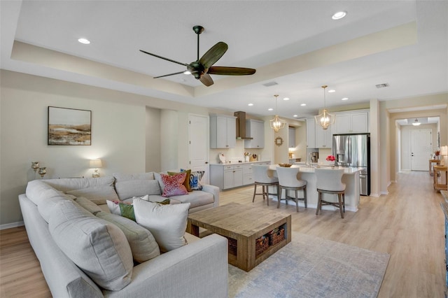 living room with ceiling fan, a raised ceiling, and light hardwood / wood-style floors