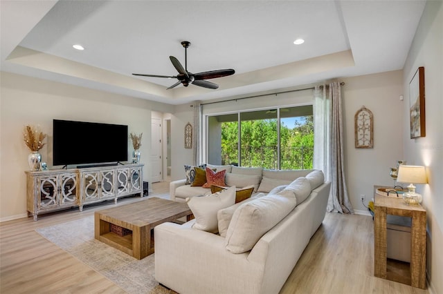 living room featuring light hardwood / wood-style flooring, a tray ceiling, and ceiling fan