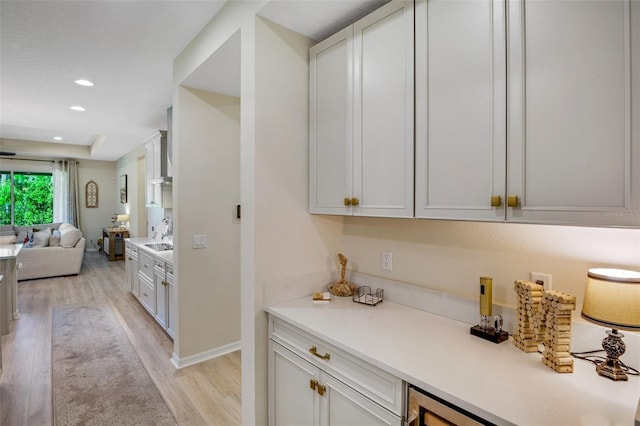 interior space featuring sink, white cabinetry, light hardwood / wood-style floors, and a tray ceiling