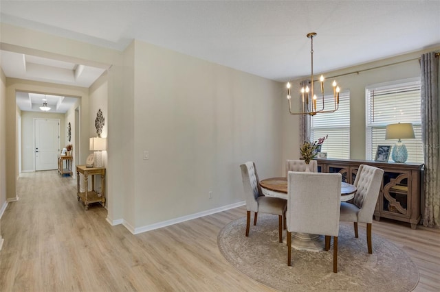 dining area featuring light hardwood / wood-style flooring, an inviting chandelier, and a raised ceiling