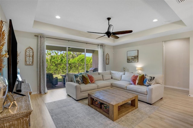 living room featuring a tray ceiling, light hardwood / wood-style flooring, and ceiling fan