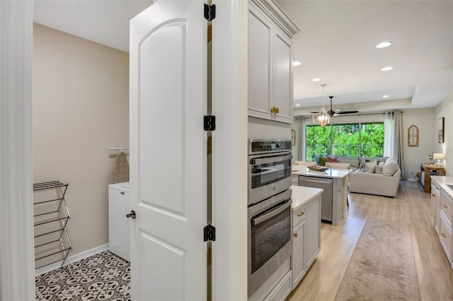 kitchen with a kitchen island, appliances with stainless steel finishes, white cabinetry, a raised ceiling, and light hardwood / wood-style flooring