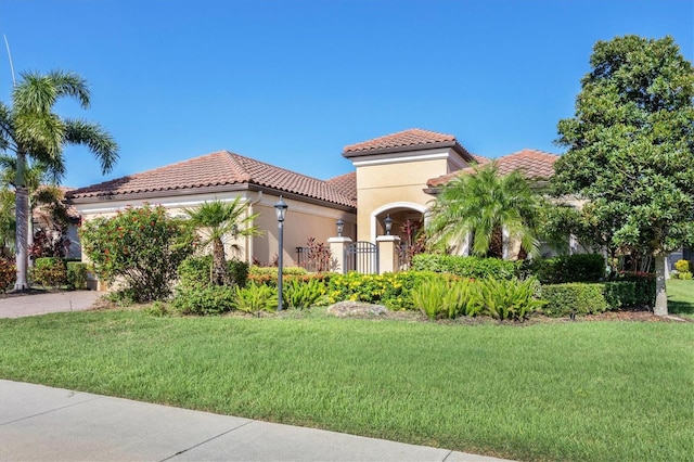 mediterranean / spanish house featuring a tile roof, stucco siding, an attached garage, driveway, and a front lawn