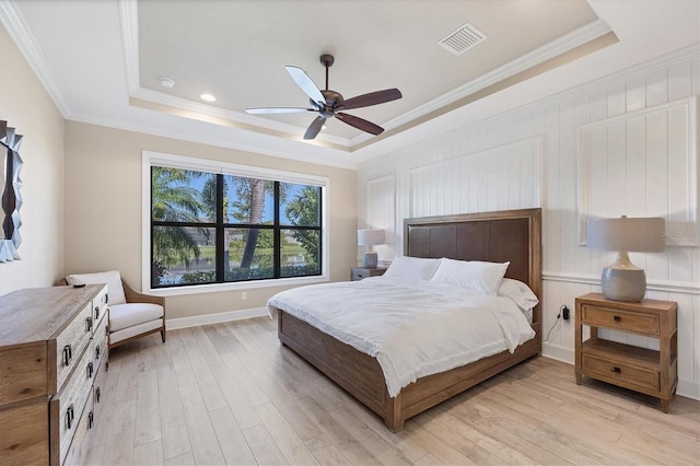 bedroom with light hardwood / wood-style floors, ornamental molding, ceiling fan, and a tray ceiling