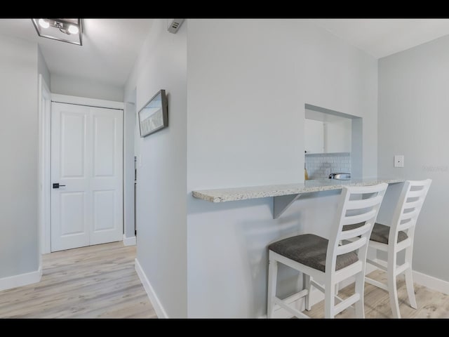 kitchen with a kitchen breakfast bar, light hardwood / wood-style flooring, decorative backsplash, light stone countertops, and kitchen peninsula