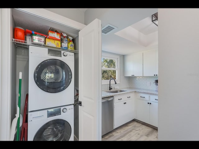 laundry area featuring light wood-type flooring, stacked washing maching and dryer, and sink