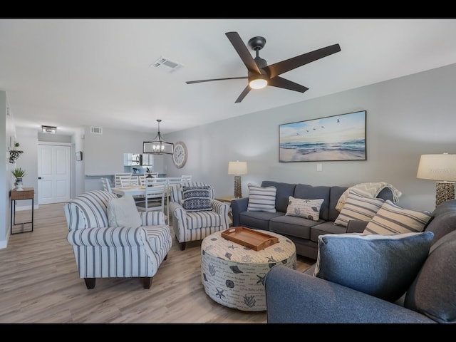 living room with ceiling fan with notable chandelier and light hardwood / wood-style floors