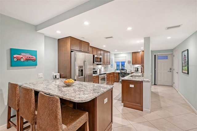 kitchen with stainless steel appliances, kitchen peninsula, sink, light stone countertops, and a breakfast bar