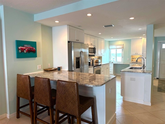 kitchen featuring kitchen peninsula, stainless steel appliances, a breakfast bar, sink, and white cabinets