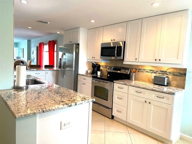 kitchen with stainless steel appliances, light stone countertops, decorative backsplash, sink, and white cabinetry