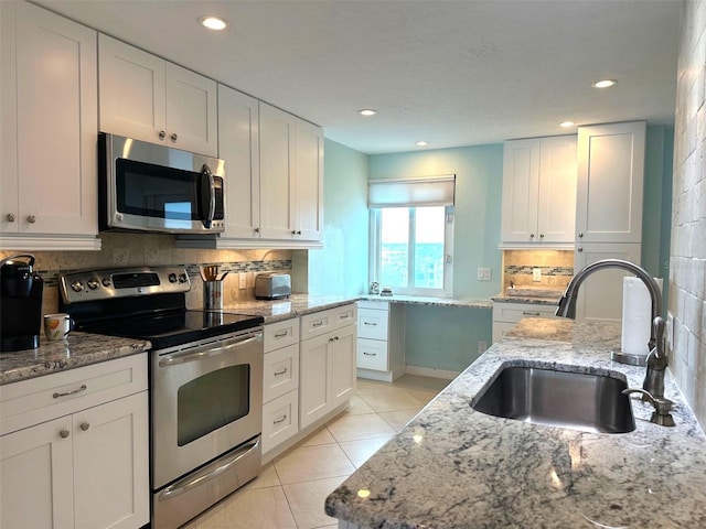 kitchen with stainless steel appliances, light stone countertops, decorative backsplash, sink, and white cabinetry