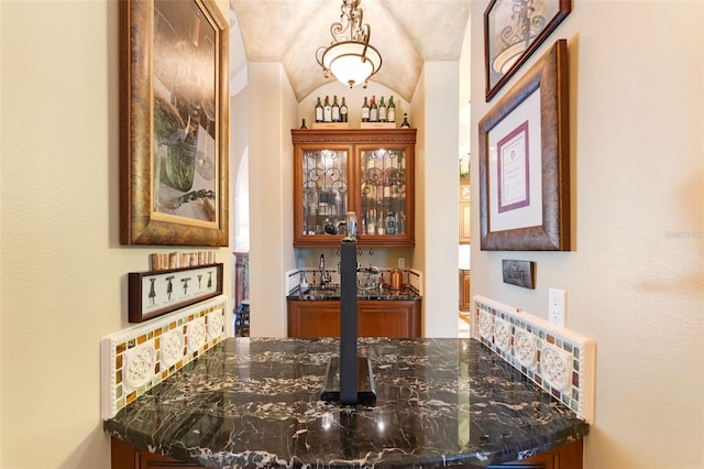 bar with dark stone counters, decorative light fixtures, and lofted ceiling