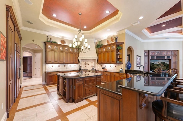 kitchen with backsplash, a breakfast bar area, a tray ceiling, a large island, and kitchen peninsula