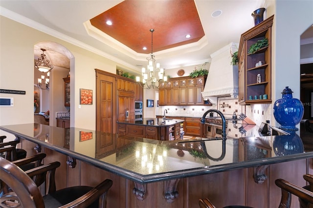 kitchen with kitchen peninsula, premium range hood, a raised ceiling, and decorative backsplash