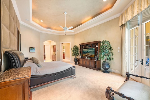 bedroom featuring arched walkways, a raised ceiling, light colored carpet, crown molding, and french doors