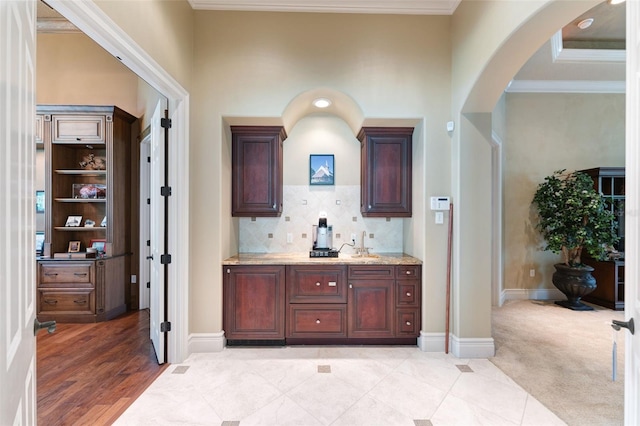 bar with crown molding, decorative backsplash, light wood-type flooring, and light stone countertops