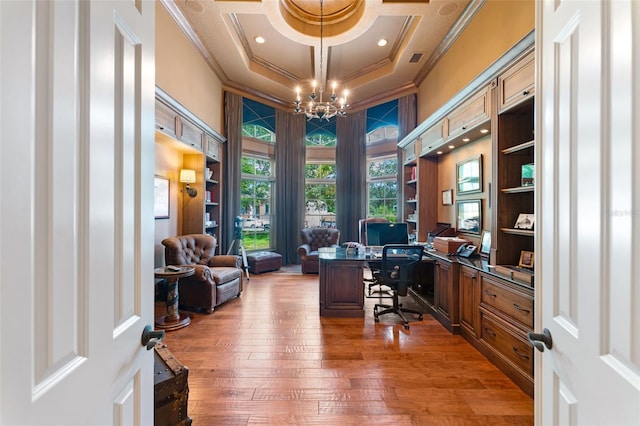 office area with ornamental molding, a raised ceiling, built in desk, wood-type flooring, and a notable chandelier