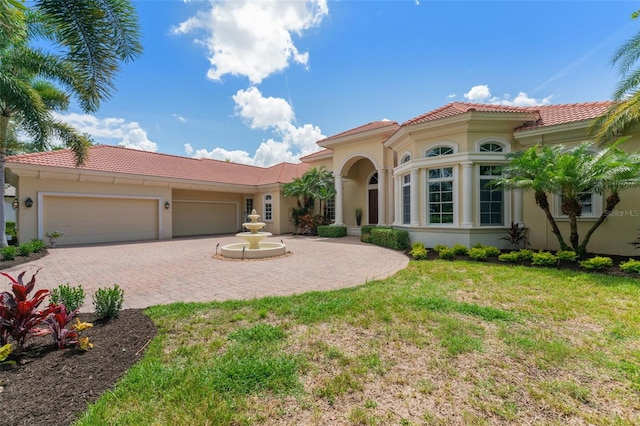 mediterranean / spanish house featuring a garage, a tiled roof, a front yard, and stucco siding