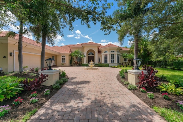 mediterranean / spanish-style home with a garage, decorative driveway, a tile roof, and stucco siding