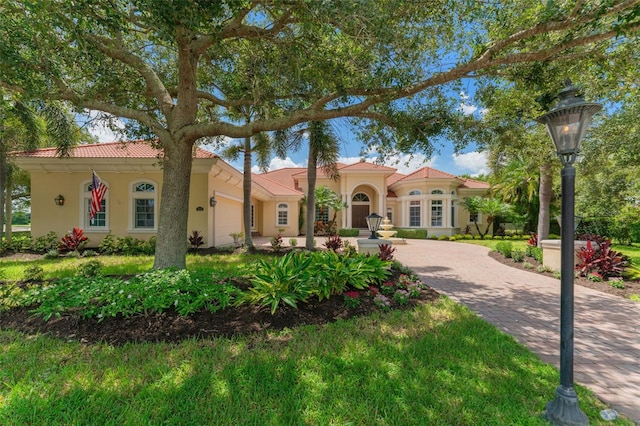 mediterranean / spanish-style home with a garage, decorative driveway, a tiled roof, and stucco siding