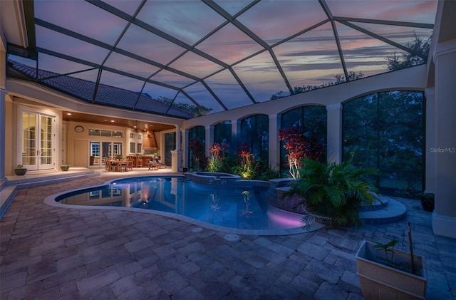 pool at dusk featuring a lanai, an in ground hot tub, a patio area, and french doors