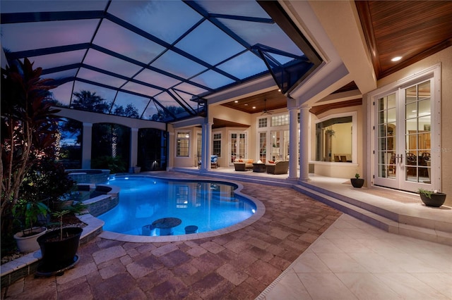 pool at dusk featuring ceiling fan, glass enclosure, a patio, an in ground hot tub, and french doors