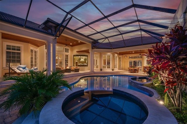 pool at dusk featuring french doors, an in ground hot tub, ceiling fan, a lanai, and a patio