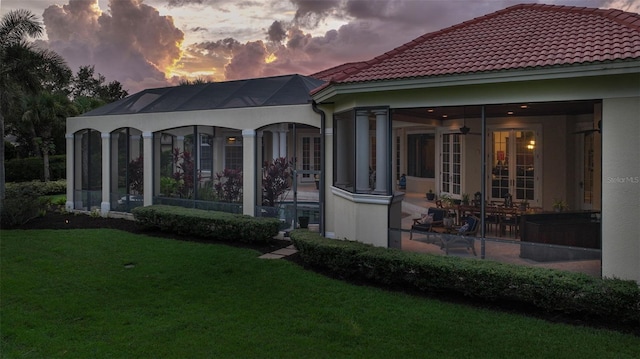 back of house at dusk featuring a yard, a tile roof, and a sunroom