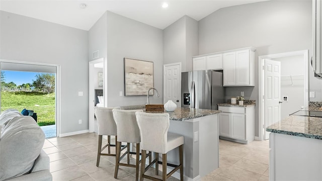 kitchen featuring light tile patterned floors, a kitchen island with sink, white cabinets, stainless steel fridge with ice dispenser, and high vaulted ceiling