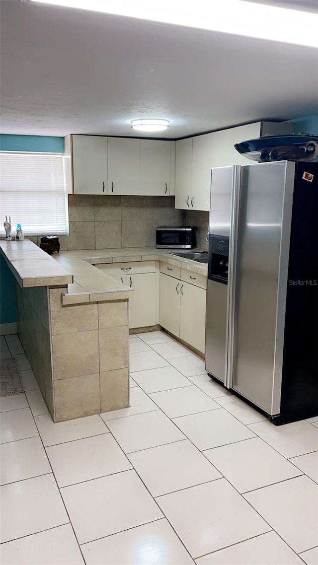 kitchen featuring light tile patterned floors, kitchen peninsula, tasteful backsplash, cream cabinetry, and stainless steel appliances