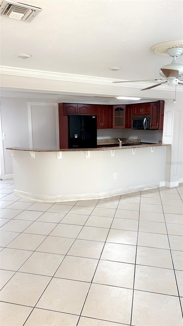 kitchen featuring a breakfast bar area, light tile patterned floors, crown molding, black refrigerator with ice dispenser, and ceiling fan