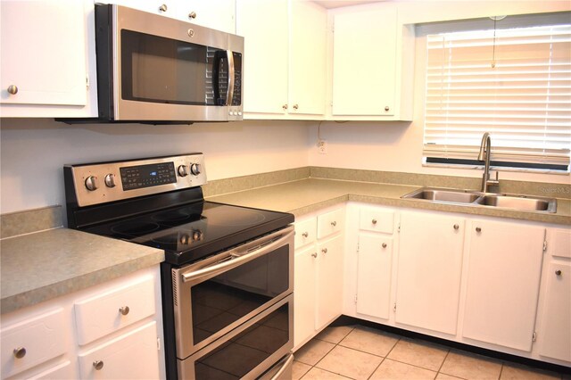 kitchen with light tile patterned flooring, appliances with stainless steel finishes, sink, and white cabinets