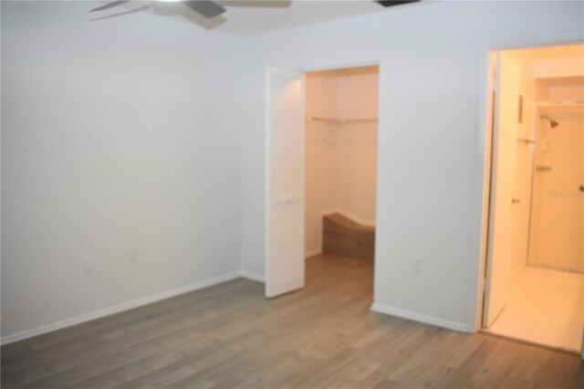 unfurnished bedroom featuring hardwood / wood-style floors, a spacious closet, a closet, and ceiling fan