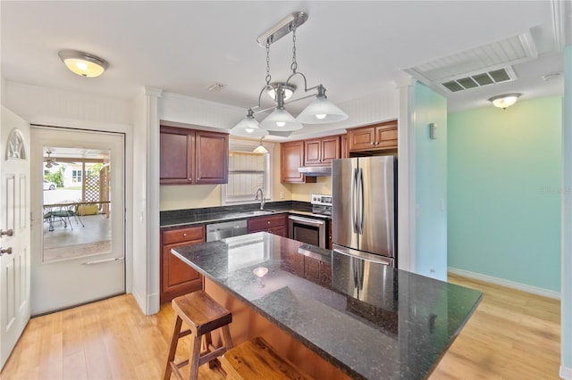 kitchen with a kitchen island, decorative light fixtures, stainless steel appliances, light wood-type flooring, and a sink