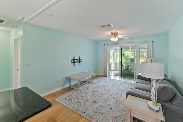 living area featuring light wood finished floors, ceiling fan, visible vents, and baseboards