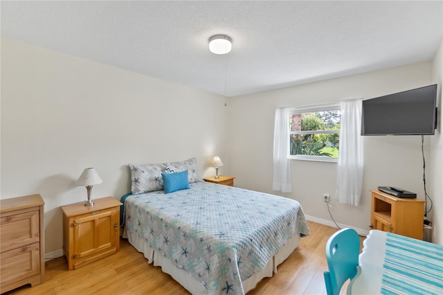 bedroom with a textured ceiling, light wood-type flooring, and baseboards