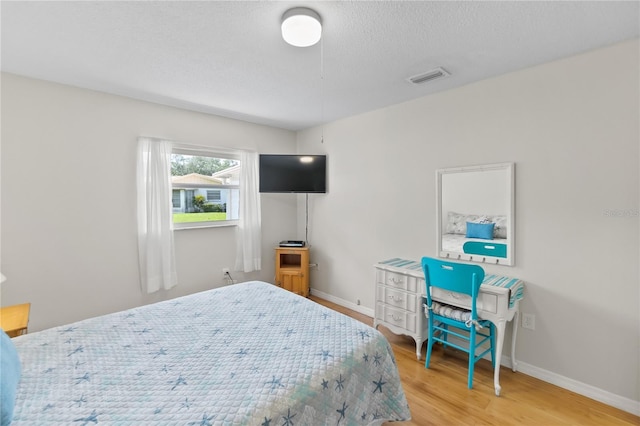 bedroom featuring light wood-style floors, visible vents, a textured ceiling, and baseboards