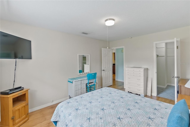 bedroom with a closet, light wood-type flooring, a walk in closet, and baseboards