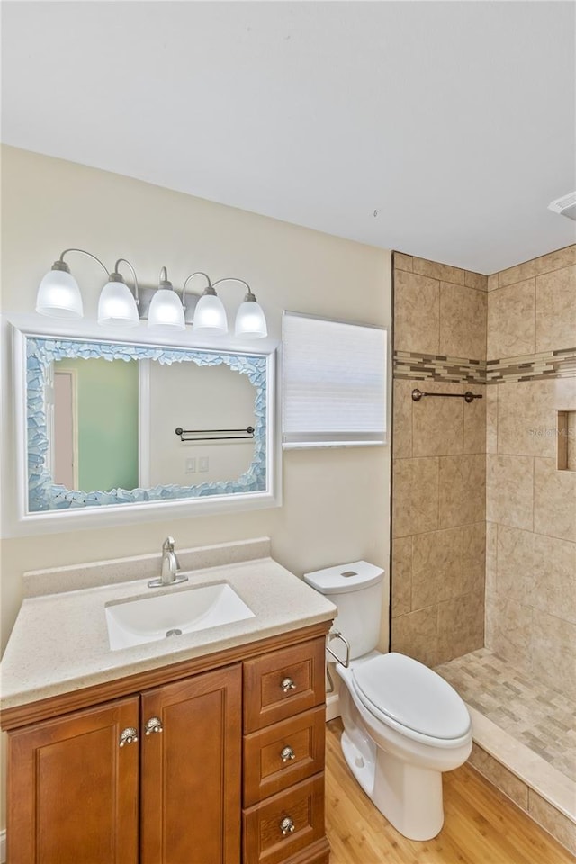 bathroom with tiled shower, vanity, toilet, and wood finished floors