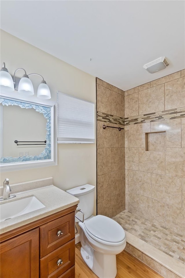 full bathroom featuring toilet, wood finished floors, visible vents, vanity, and tiled shower