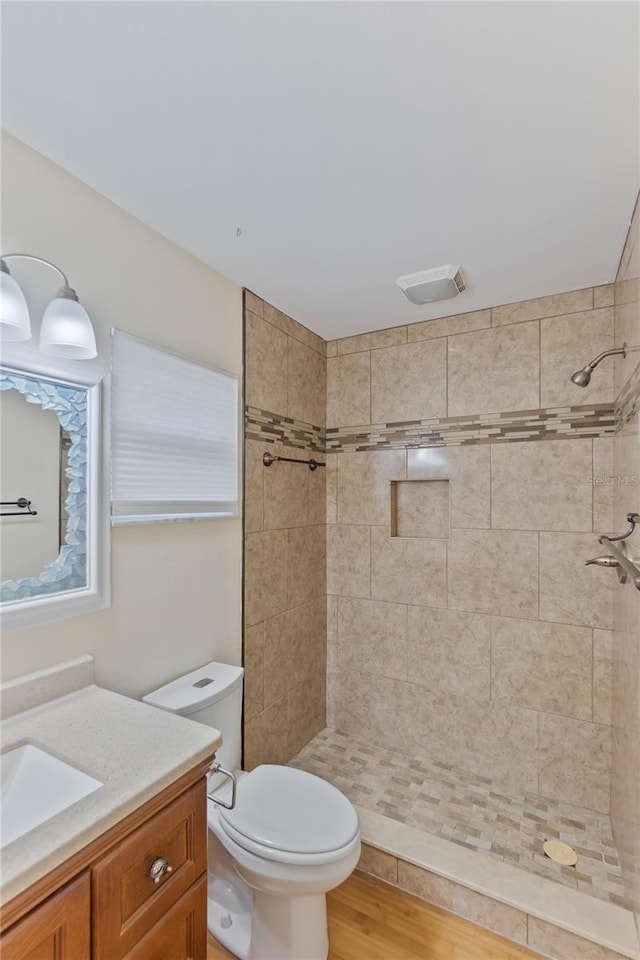 bathroom featuring toilet, wood finished floors, vanity, and a tile shower