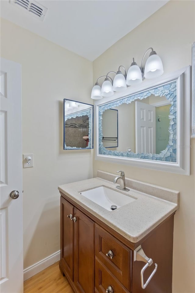 bathroom with visible vents, vanity, baseboards, and wood finished floors